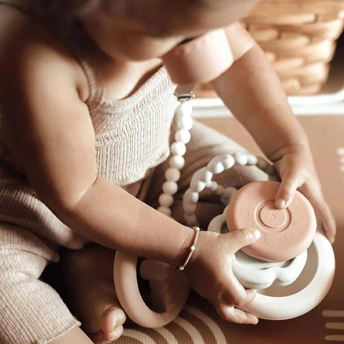 An infant engaging with the Ali + Oli Soft Silicone Stacking Ring Tower on a soft rug