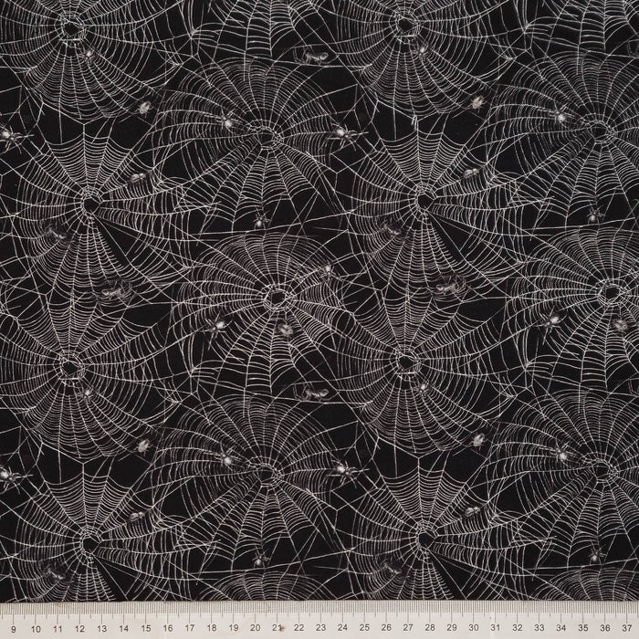 Black fabric with a repeating white spiderweb pattern, shown flat with a white ruler along the bottom edge for scale.