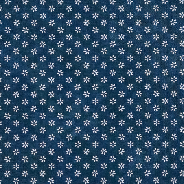 A close-up of a dark blue cotton quilting fabric with a repeating white floral or starburst pattern.