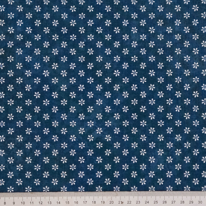 A close-up of a dark blue fabric with a repeating pattern of small white flowers, with a white ruler visible along the bottom edge for scale.