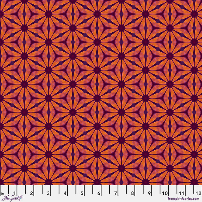 A floral geometric pattern in reds and oranges printed on a cotton quilting fabric with a cm ruler