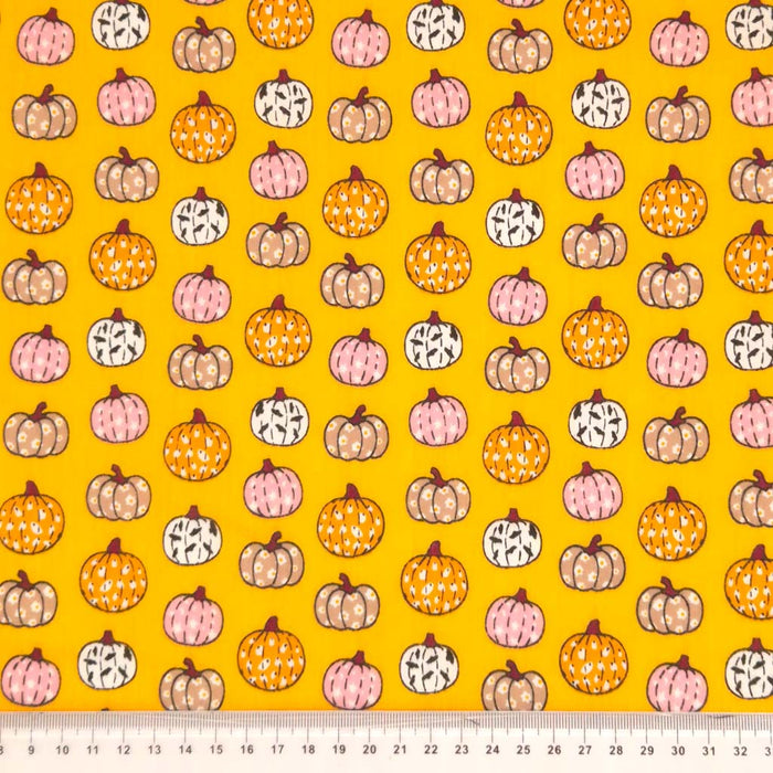 Ditsy decorated pumpkins are printed on an orange polycotton fabric for halloween with a cm ruler