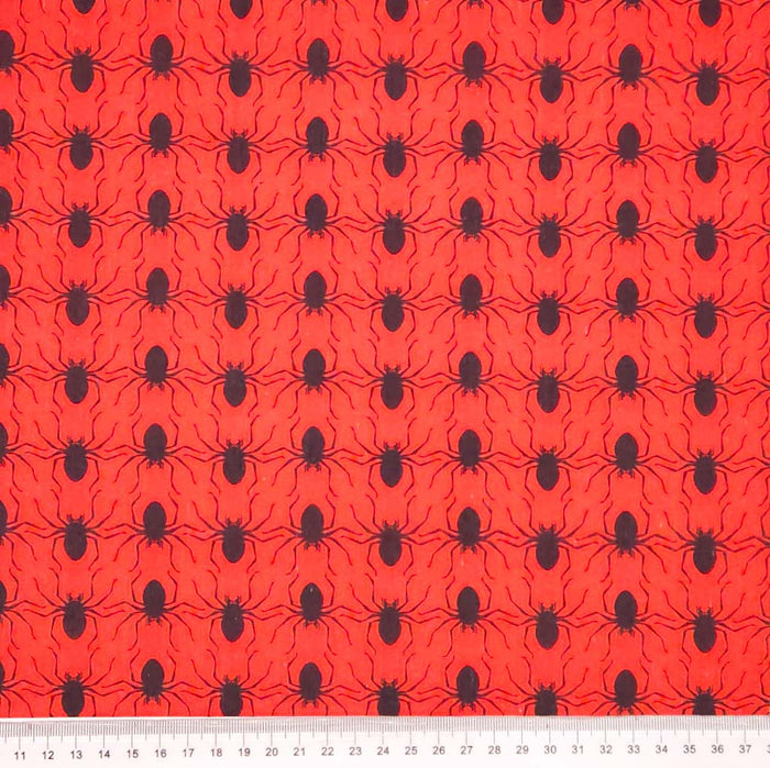 Red halloween polycotton fabric with black spider pattern and a ruler at the bottom for scale.