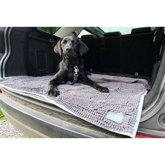 A black dog laying on the Henry Wag Microfibre Noodle Pet Mat, in the back of a car boot.