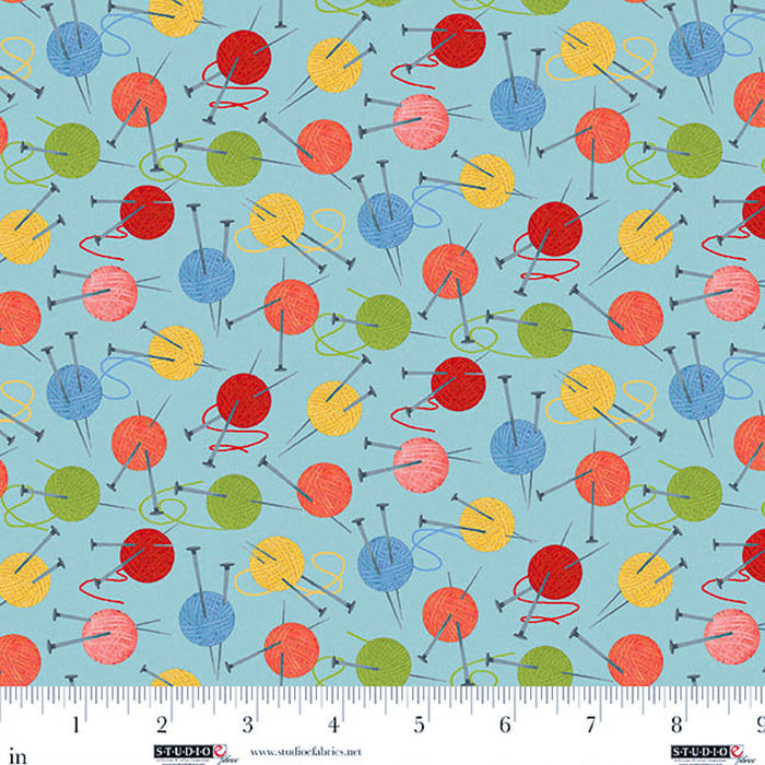 Colorful pattern of wool balls and knitting needles on a blue background with a ruler at the bottom.