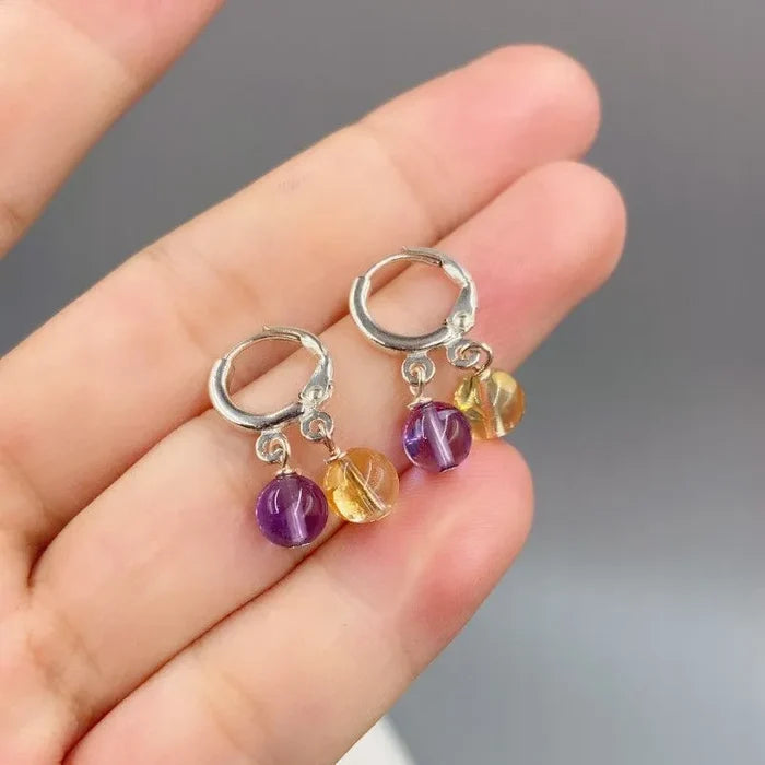 Hand holding natural amethyst and citrine S925 silver earrings fingers close-up, Crystalvana