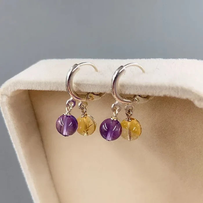 Amethyst and citrine S925 dangle earrings flat lay on wood slice with flowers, Crystalvana