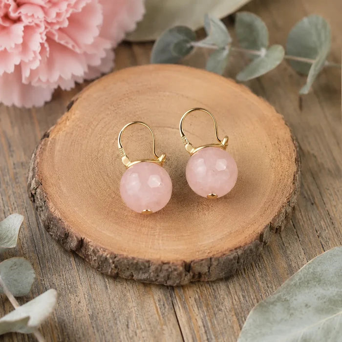 Natural rose quartz S925 silver buckle earrings flat lay on wood with eucalyptus and pink carnation, Crystalvana