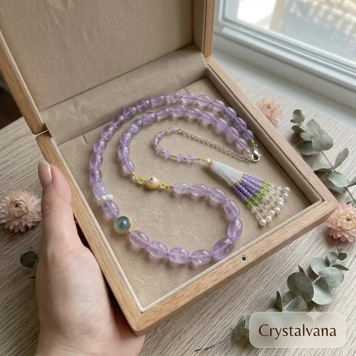 Lavender amethyst necklace with tassel pendant held in hand showing evil eye charm detail, Crystalvana