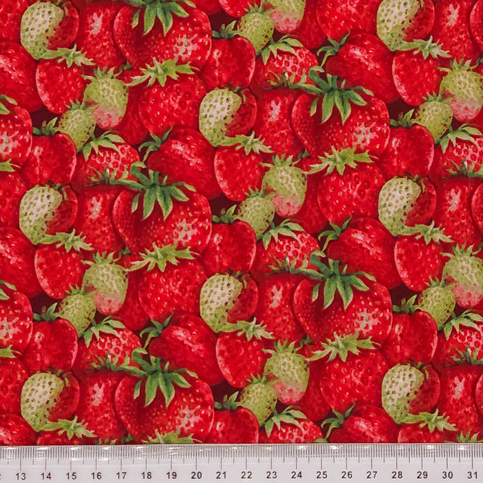 Fabric with a pattern of red strawberries and green leaves, with a ruler at the bottom for scale.