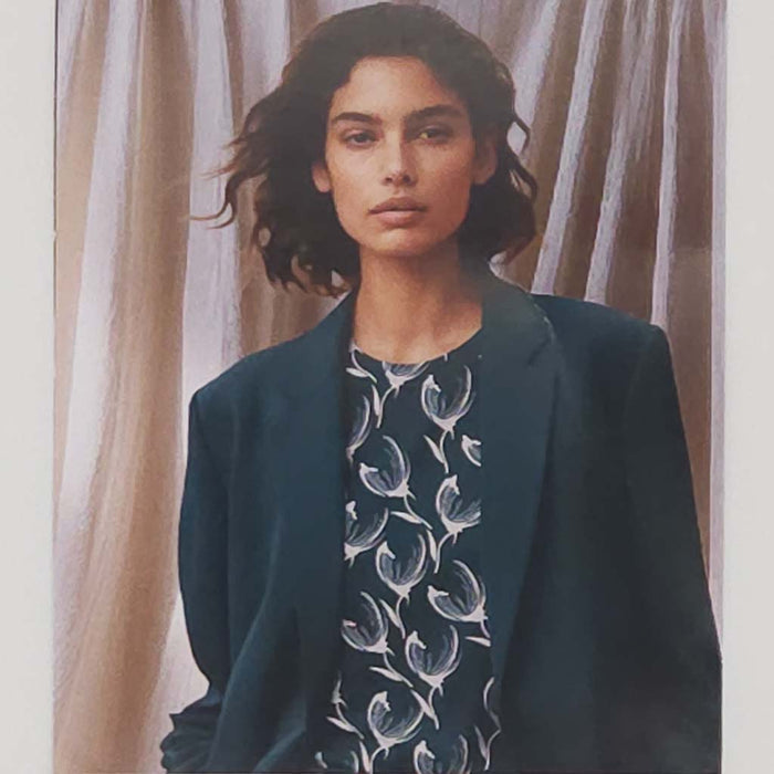 Woman wearing a dark blue blazer over a patterned shirt with a neutral background