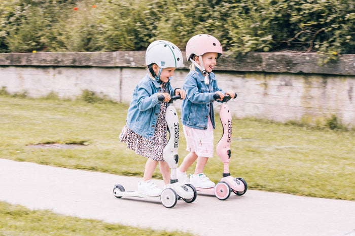 Two kids safely wearing helmets while riding their Scoot & Ride scooters outdoors