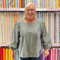 Person wearing a patterned shirt and blue pants standing in front of fabric shelves.