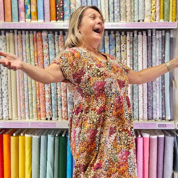 Woman in a colorful dress standing in front of fabric shelves with various patterns and colors.