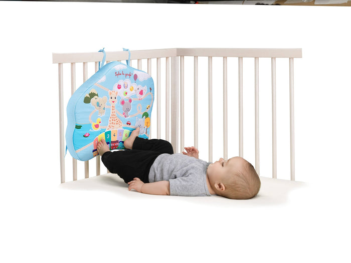 Baby lying in a crib using his feet to play with Sophie la Girafe Touch & Play Board