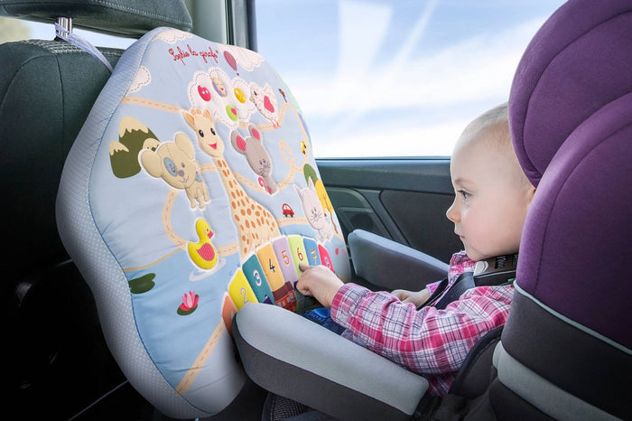 Child in car seat playing with Sophie la Girafe Touch and Play Board hanging from the back of the headrest.