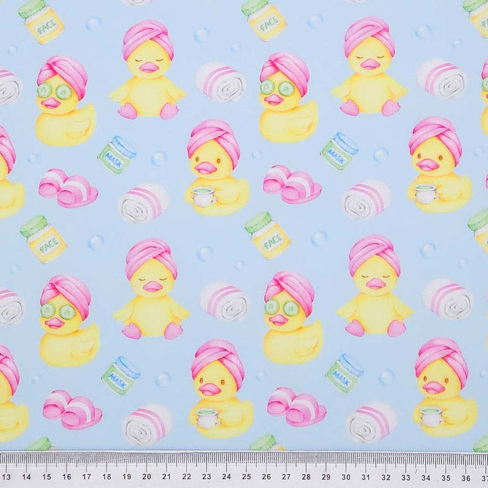Pattern of yellow rubber ducks with pink towels and jars on a blue polycotton fabric with a ruler