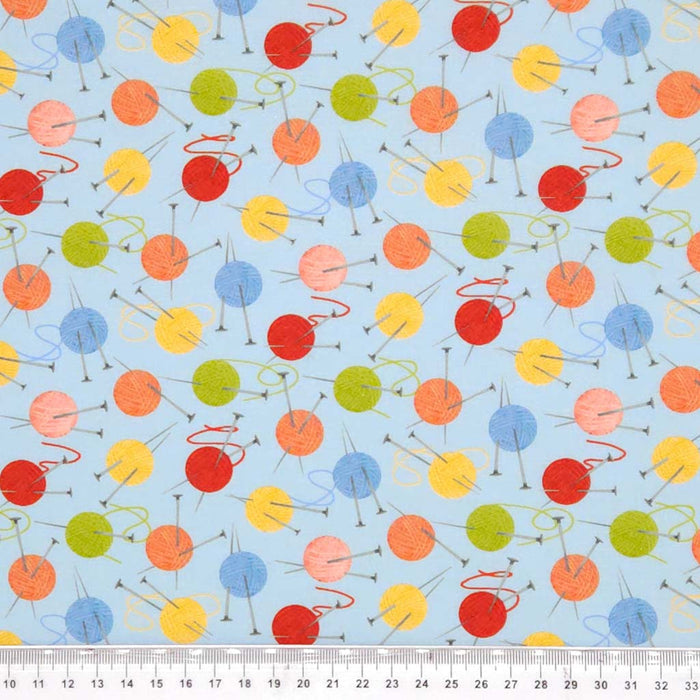 Balls of wool and knitting needles printed on a blue cotton fabric with a cm ruler
